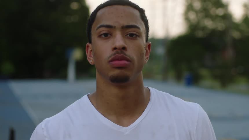 Young man wearing white shirt standing outdoors at evening looks up to the camera
