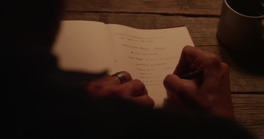 A man writes in a book with a small pencil