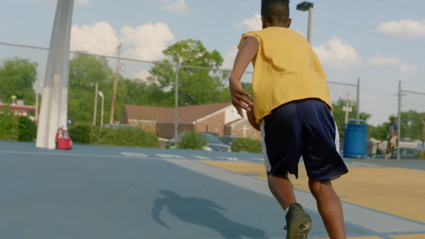 A boy in a basketball court dribbling a basketball towards a basketball hoop