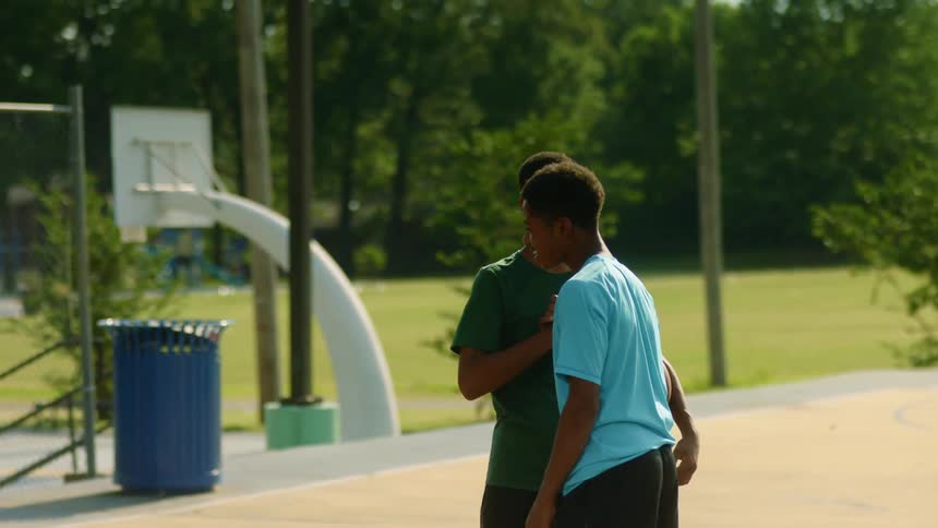 Two teenage boys shake hands outside on a basketball court