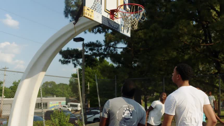 Group of young men playing basketball in a public court on a sunny day
