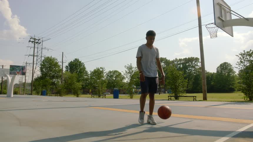 A teenage boy dribbling a basketball outside