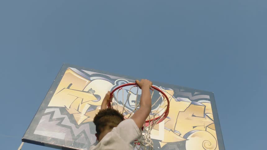 A boy dribbles towards an outdoors basketball hoop and is lifted by a man so that he can dunk the basketball