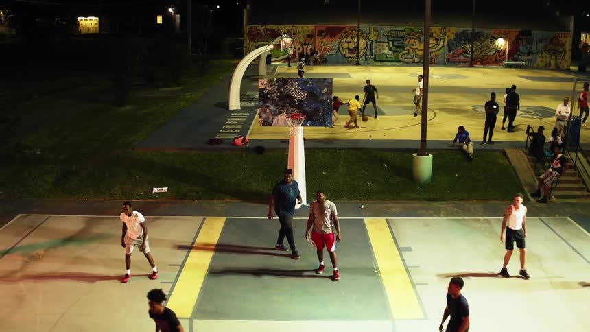 Two basketball courts outside with groups of teens playing and people watching on the sidelines