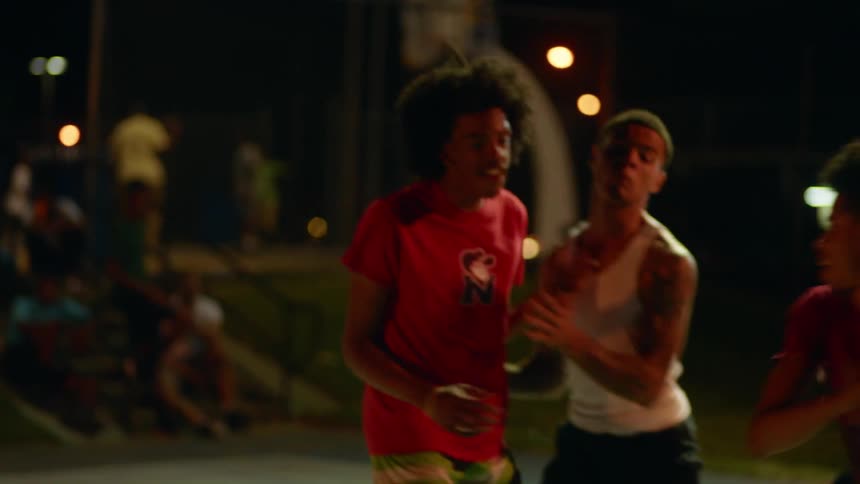 A group of teenage boys playing basketball outside at night