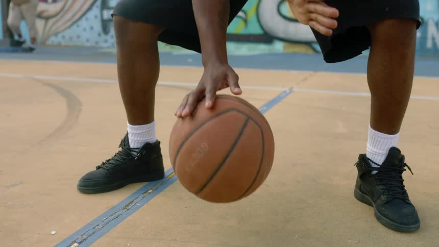 Young man dribbles a basketball on a court near a wall filled with graffiti