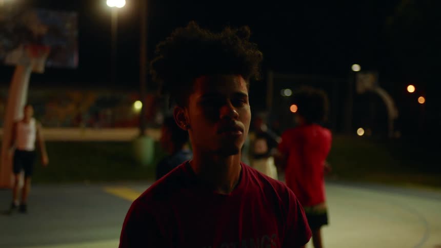 A man standing on a basketball court with people and lights behind him