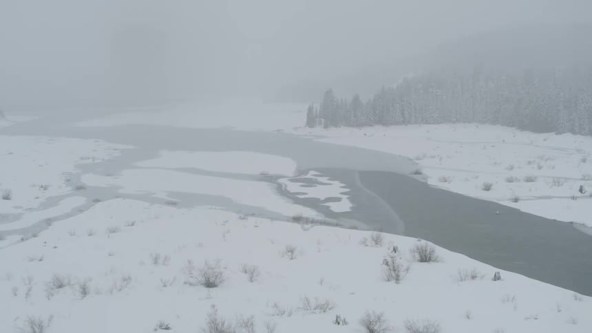 A river starts to ice over along a snowy meadow during a blizzard