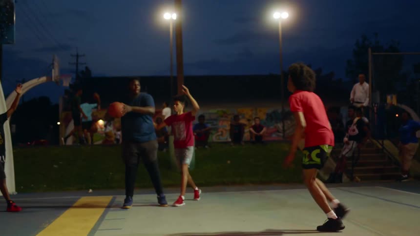 Group of black men play basketball outdoors at night