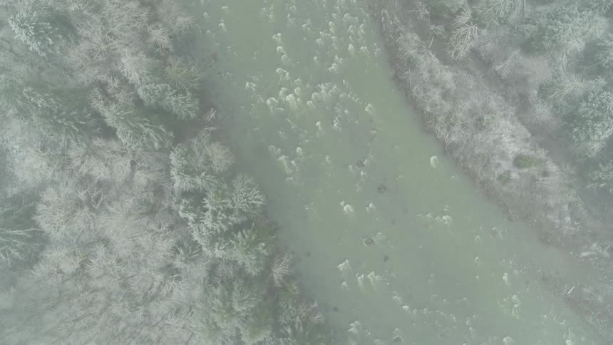 Birds eye view of a river flowing through a misty forest during a snow storm