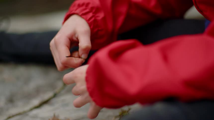 A little girl sitting outside places leaves on the cement where she sits