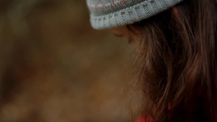 Teenage girl wearing red jacket and grey hat plays in the ground outdoors