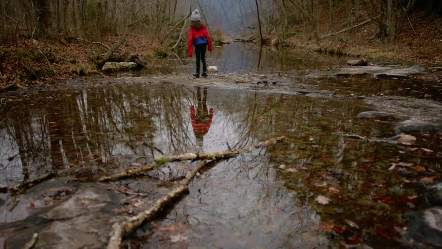 Girl walks to stand in middle of stream looking toward foggy area