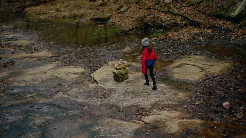A young girl walks down by a steam and picks up a rock
