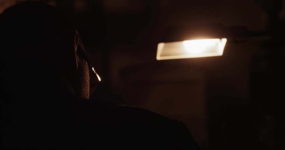 A man sits in a dark room under a light