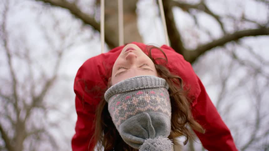 A girl laying on her back on a tree swing opens her eyes for a moment before closing them again