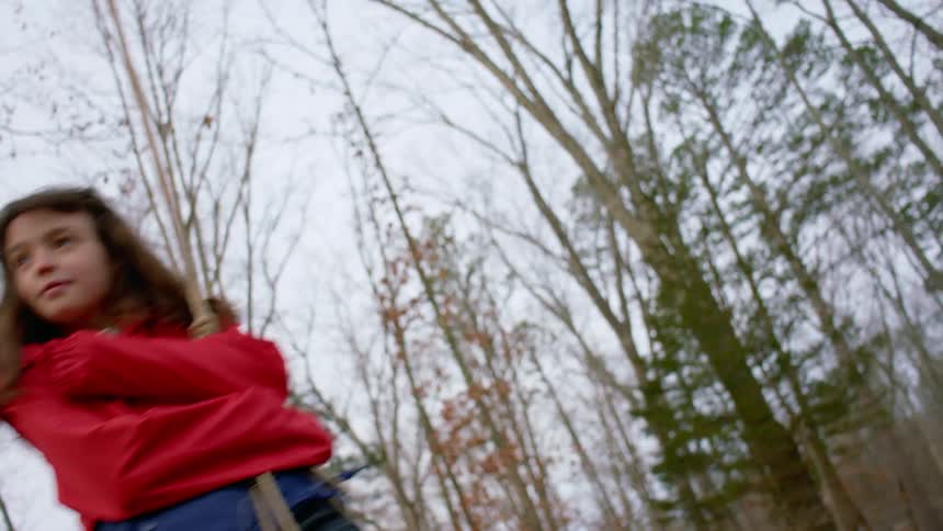 A young girl stands and swings on a rope swing
