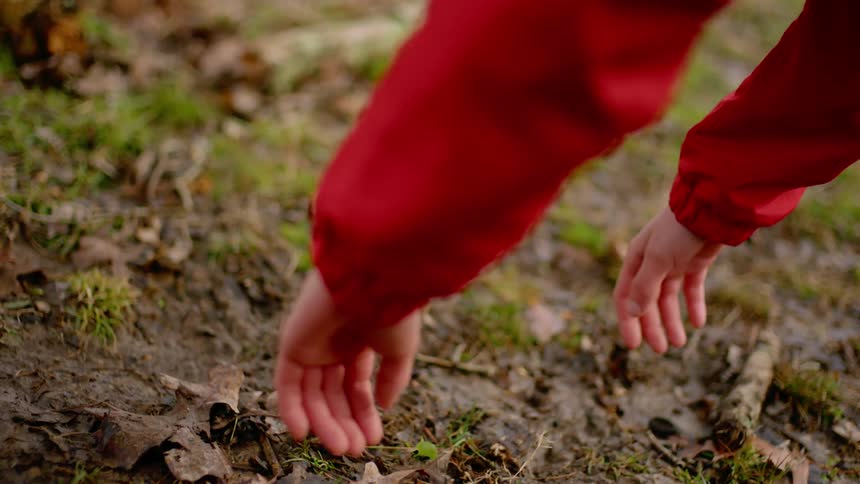 A persons hands hanging over the ground with grass leaves and mud