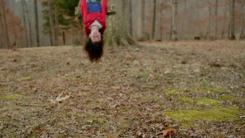 A little girl on a swing in the forest leaning back so far her hair touches the ground