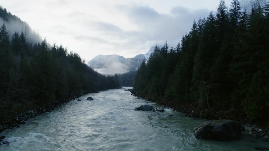 Flying upstream down through the mist above a fast flowing mountainside river