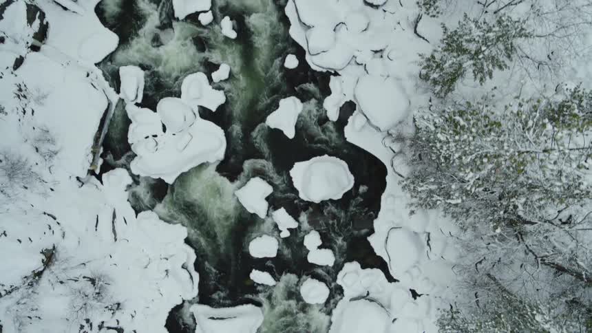 Flying over whitewater rushing down a icy river along a steep mountainside