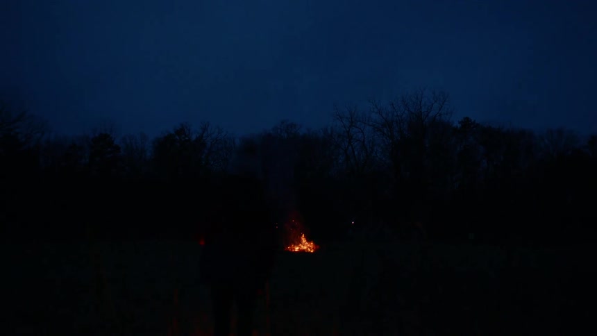 A person carrying a lantern walks towards a fire pit