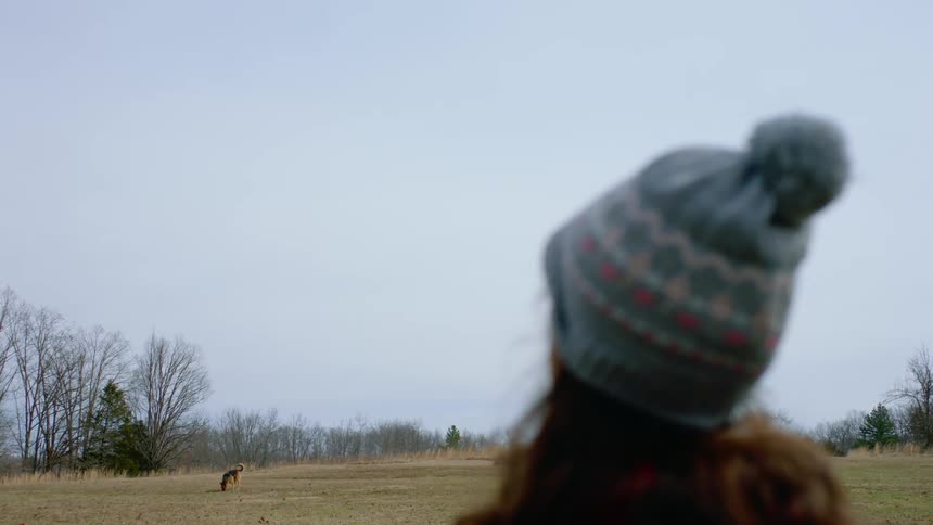 A female in a field watching her dog walk around