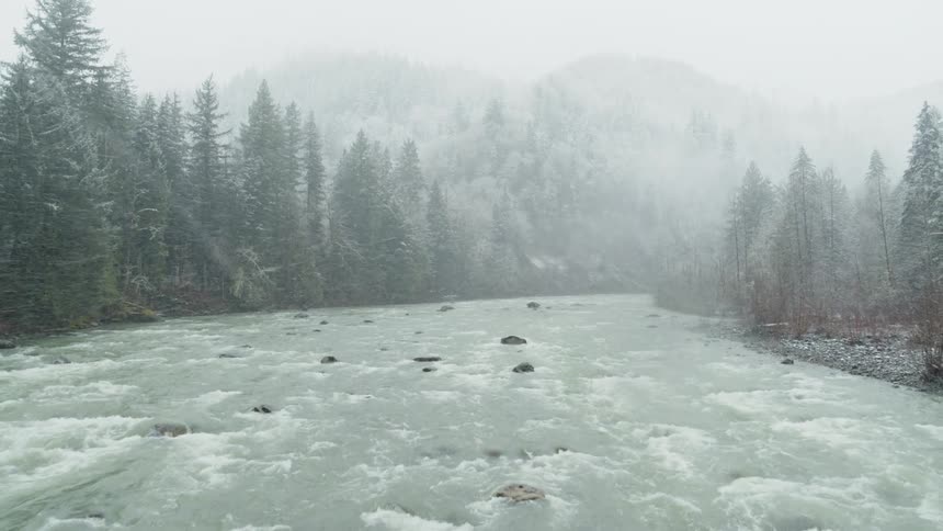 Skimming over a wide churning river during a mountain snow storm