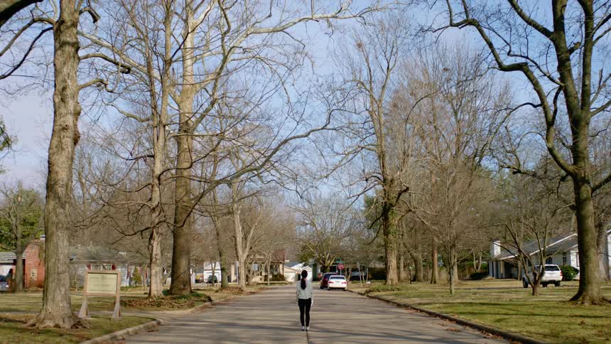 A woman slowly walks in the middle of the road in a small suburban home area