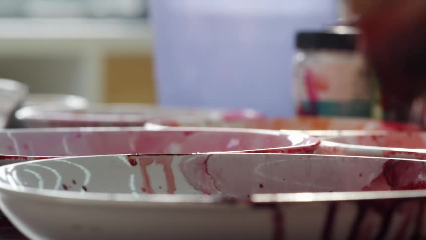 A painter mix colors on shallow ceramic bowls with a brush