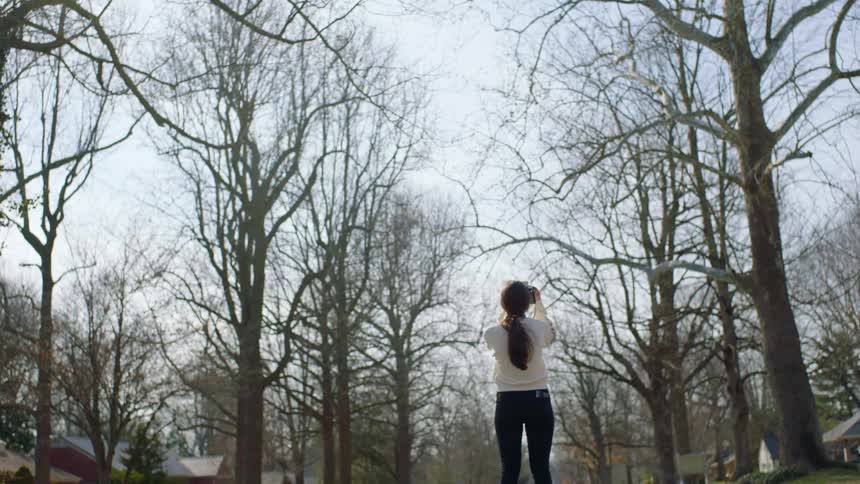 Woman takes polaroid pictures of the trees in the streets of the neighborhood