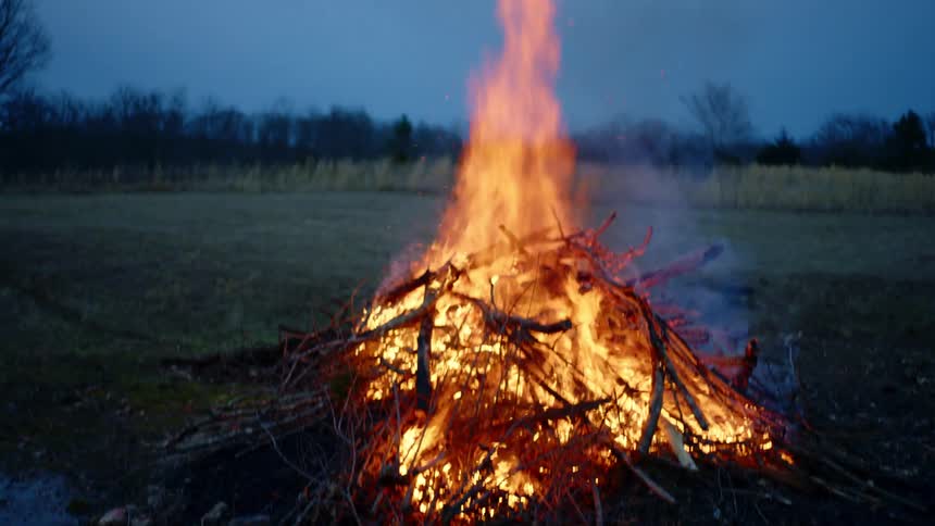 A bonfire burning next to a river and field
