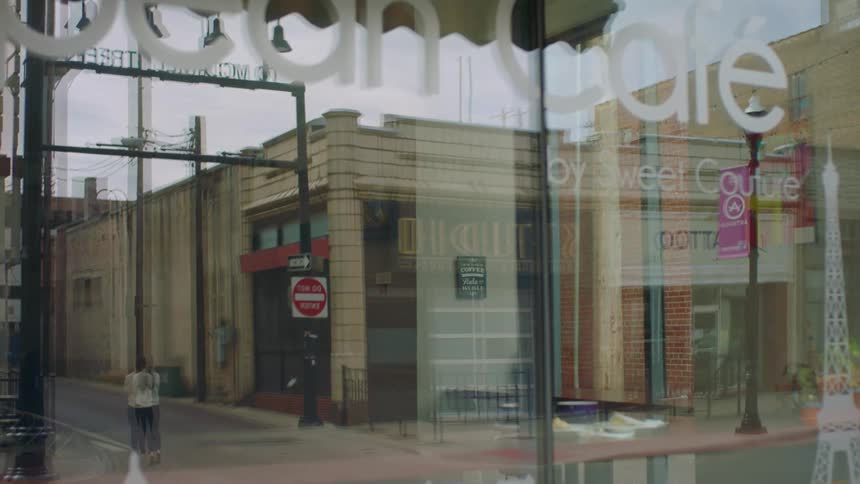 A large shop window reflects a woman crossing the street at a city intersection