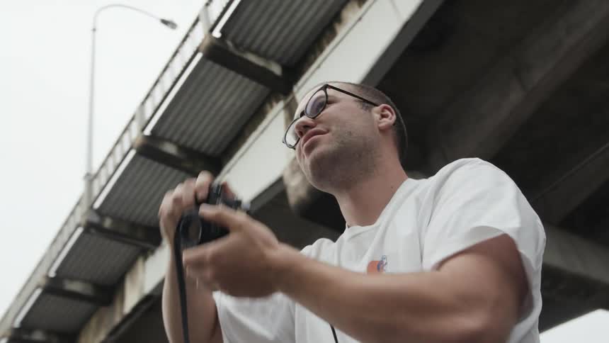 A photographer takes a photograph with his camera while standing under a bridge during the day