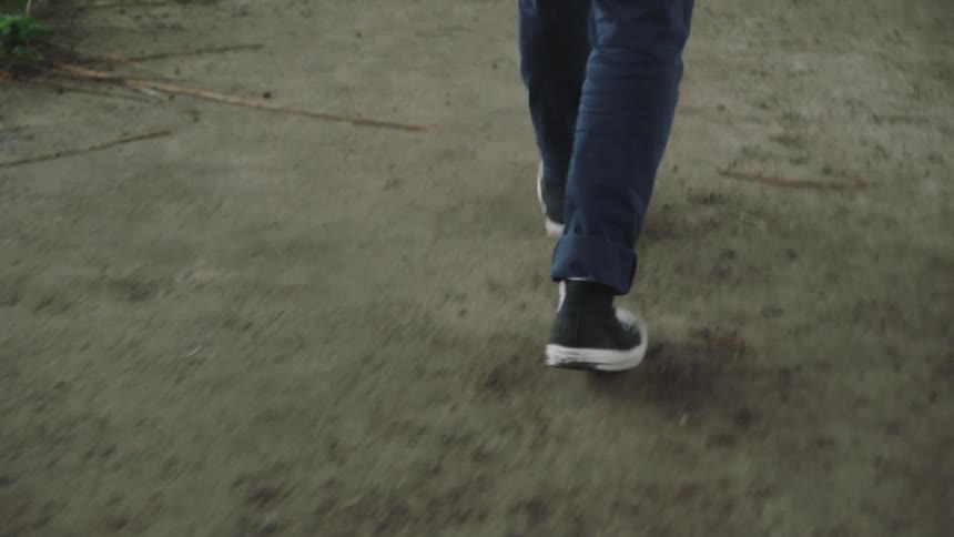 Person wearing sneakers and jeans stands on sandy ground then turns and walks