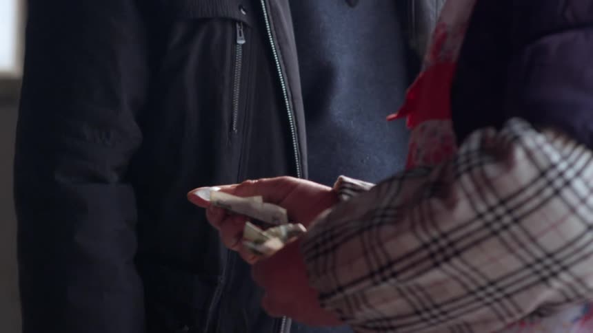 A man gives money to another man as he walks past on the street