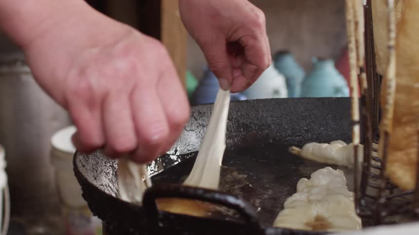 A chef frying dough in a cast iron pot of hot oil