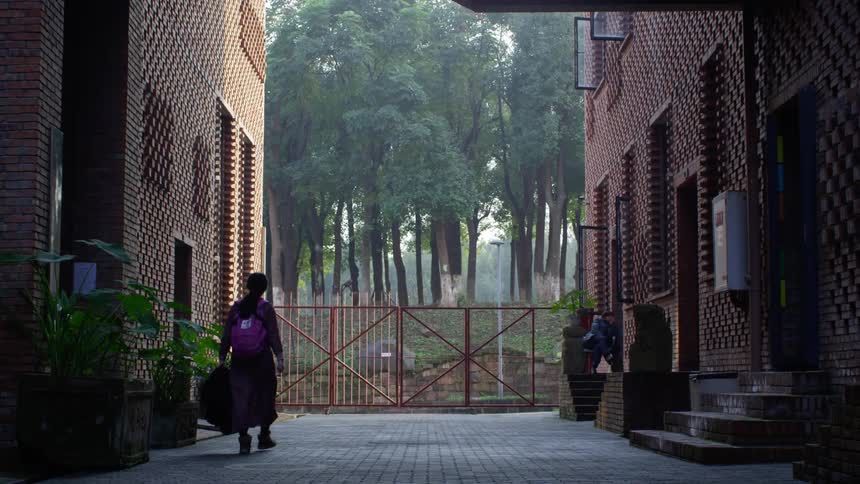 A teenage girl walks home between two apartment buildings where a teenage boy is sitting on a stoop