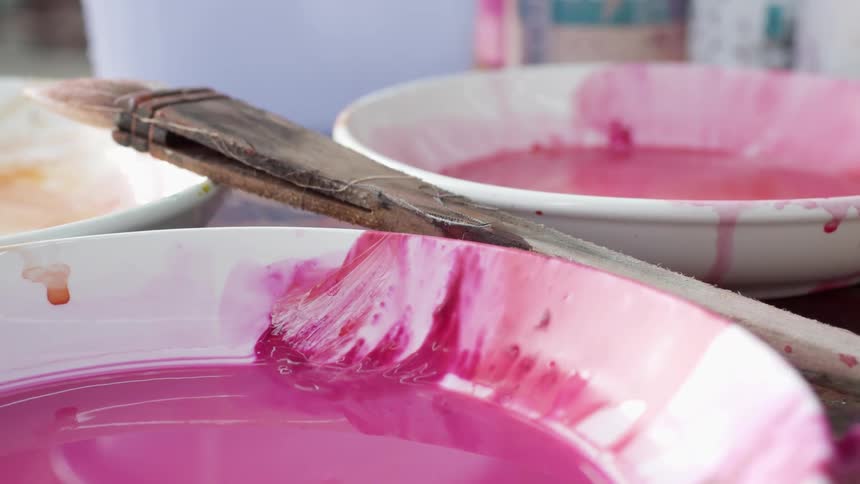 A paint brush rests on bowls of paint