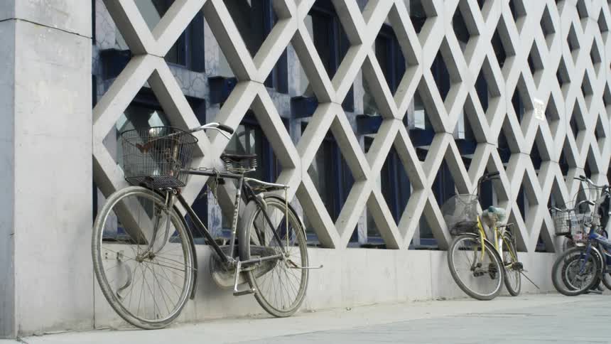 Bicycles are locked to a building with a concrete honeycomb style facade