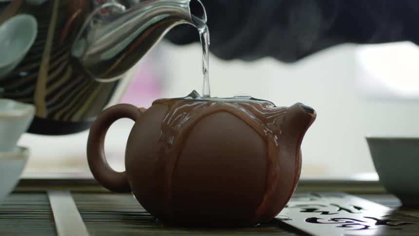 Man with bruised knuckles pours hot water into tea pot until it overflows then tops it with lid