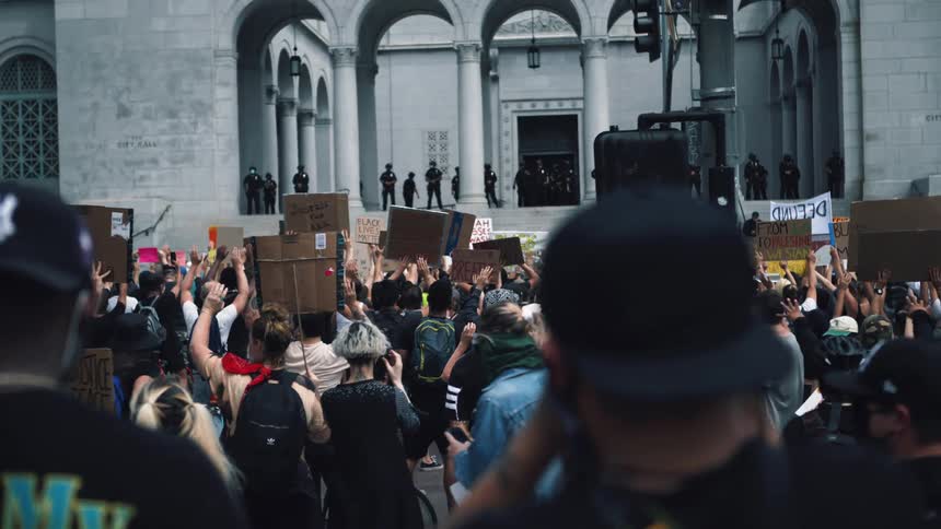 A large group of people crowd closely together for a protest in front of military and law enforcement
