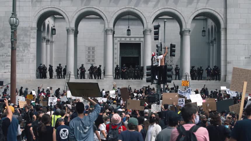 A huge crowd of people protest in front of police near a government building