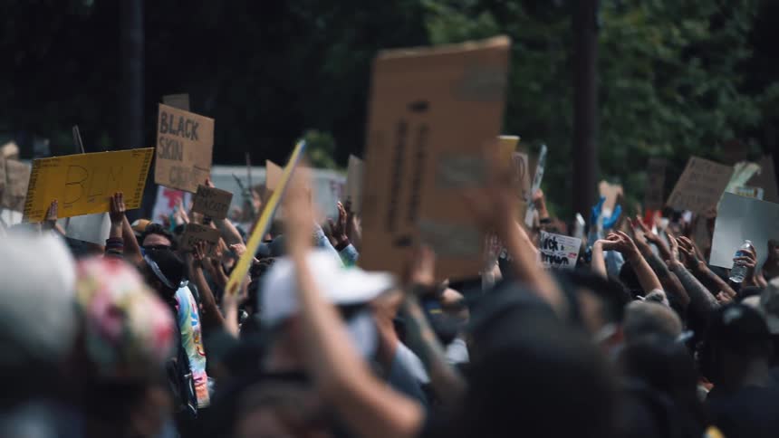 Male wearing a facial mask walking through crowd of protesters