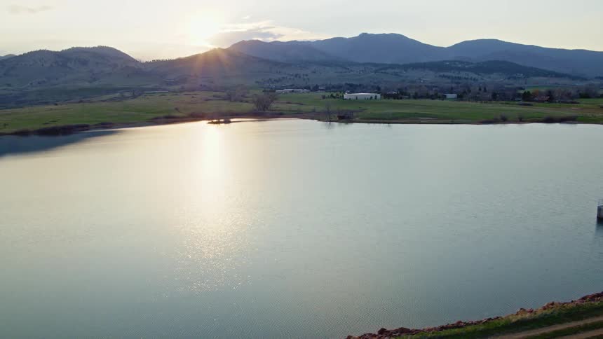 Aerial view of a lake reflecting the sunlight filtering through the mountain peaks at sunset