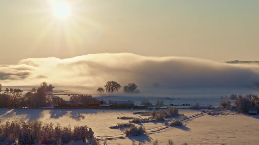 The sun shines on the snow covered hills and land as a vehicle travels on a road