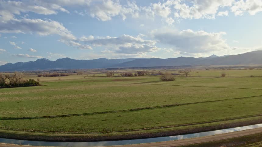 Aerial view of a grass field near a mountain range under the white clouds at morning
