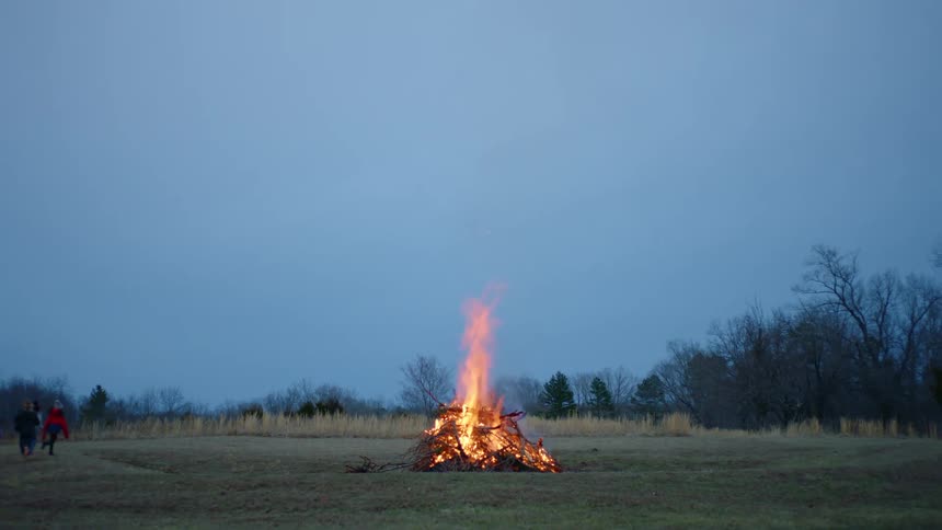 A group of people run around in a field with a large bonfire
