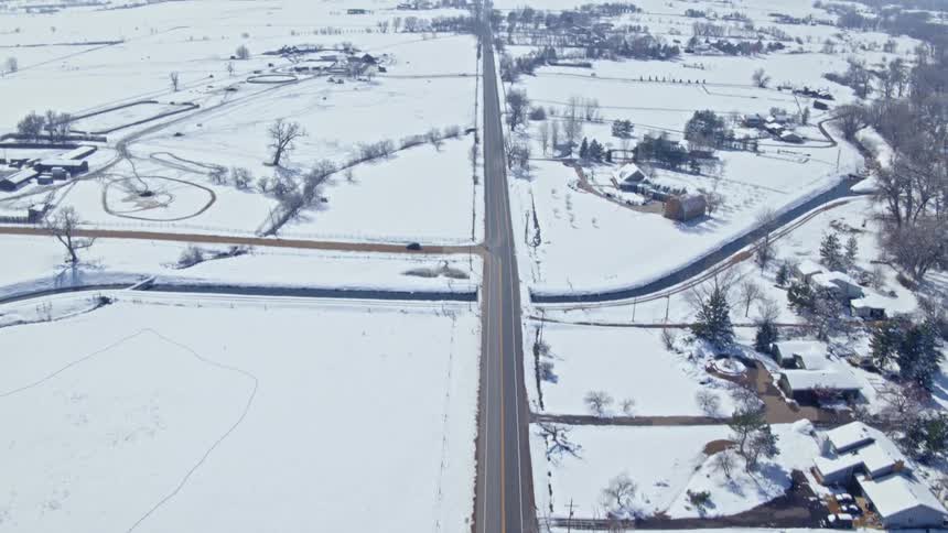 Aerial view of a small town covered in white snow on the plains next to the mountains on a clear winter day