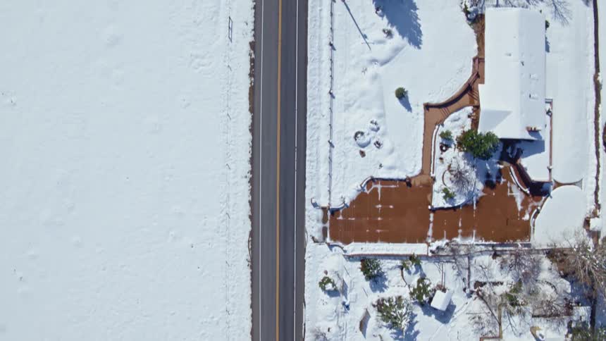 Top down aerial view of a road in a neighborhood covered in snow